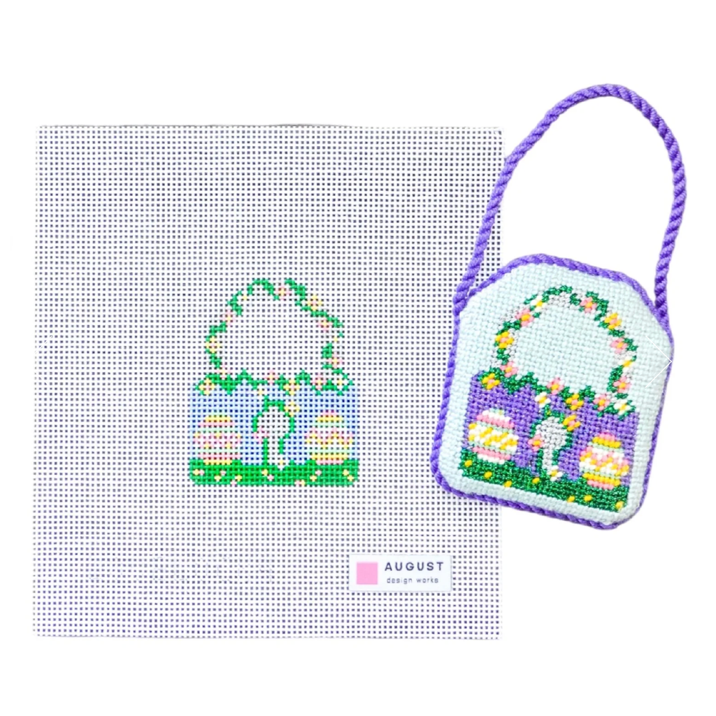 Cross-stitched design of a handbag with flowers on a white background, featuring the brand 'August'.